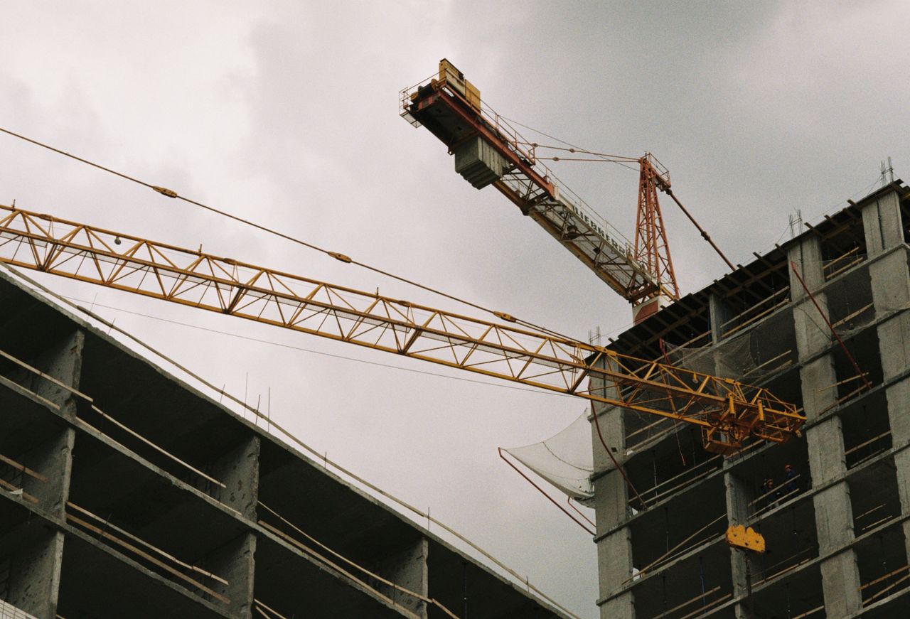 A tower crane at a high-rise construction site under a cloudy sky.
